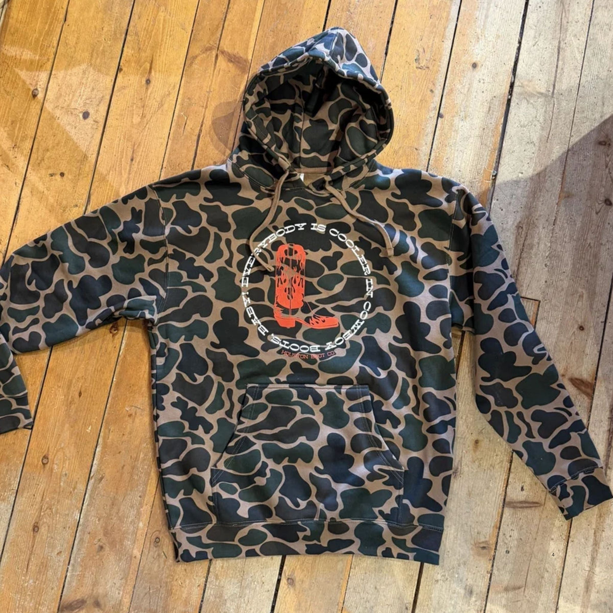 Houston Boot Co branded camo hoodie laying on wooden bench